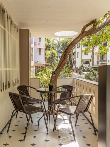 Covered balcony with round table, rattan chairs, patterned floor and a tree growing through a circular skylight