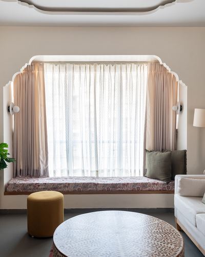 Curved plaster window nook with sheer curtains, cushioned seat, and mustard pouf in living room