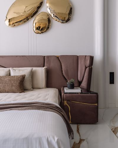Mauve velvet paneled headboard with gold sculptural wall art and marble-top nightstand in bedroom