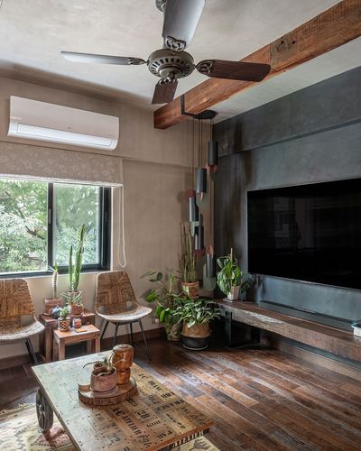Rustic living room with wood beam, cane chairs, plants, and dark metal-clad tv wall