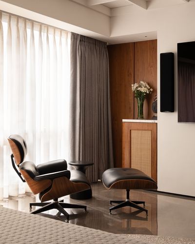 Black leather lounge chair and ottoman by sheer curtains near wood cabinet with flowers