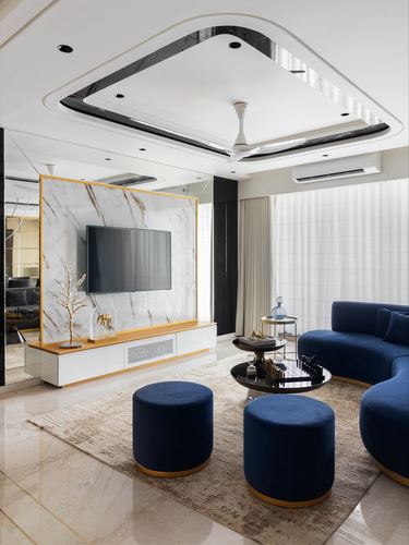 Living room with curved navy velvet sofa, marble-look gold-framed TV wall, and layered white ceiling