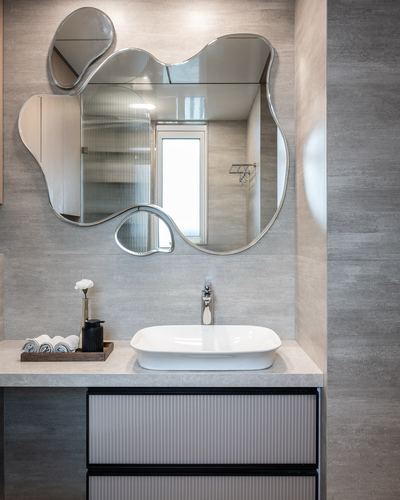 Bathroom vanity with an amoeba-shaped mirror above a white vessel sink on a stone counter
