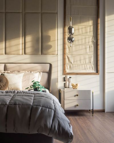 Bedroom with tufted fabric wall panels, grey bedding, and a nightstand lit by raking sunlight