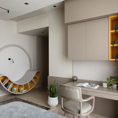 Beige study nook with circular arched bookshelf, desk, and mustard-lit display cabinet