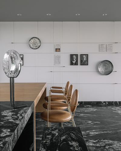 Dining nook with black stone floor, tan leather chairs, and a wall displaying plates and portraits