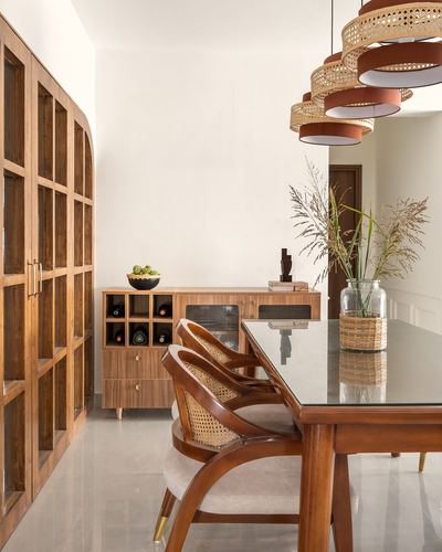 Wooden dining room with cane chairs, glass-top table, arched wardrobe doors and layered rattan pendant lights.