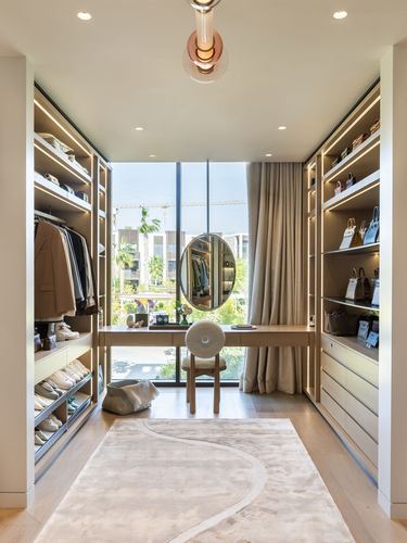 Symmetrical walk-in closet with lit shelving, vanity, round mirror, and city view window