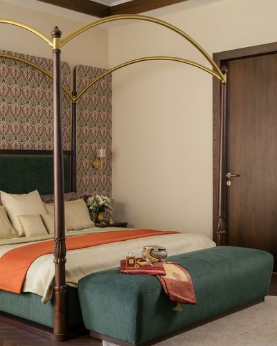 Four-poster bed with brass arched canopy, green velvet headboard, and patterned wallpaper backdrop