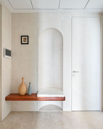 Arched plaster niche with cushioned seat beside a floating wood bench holding two vases