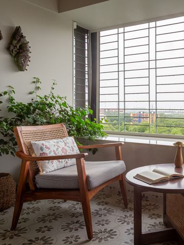 Cane armchair and round wood table on patterned tile floor by a grid-paned window with plants