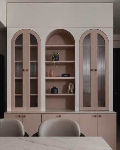 Symmetrical blush pink cabinetry with arched fluted-glass doors and open display niche
