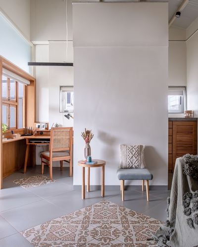Study nook with cane chair and wooden desk beside a plain column, patterned floor tiles in foreground.