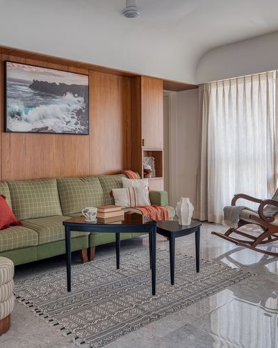 Living room with green plaid sofa, wood-panelled wall, seascape art, and cane rocking chair