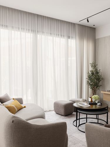 Neutral living room with curved beige sofa, sheer curtains, and nested round coffee tables