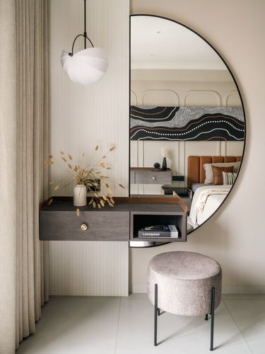 Floating wood console with round mirror reflecting a bedroom with patterned headboard artwork