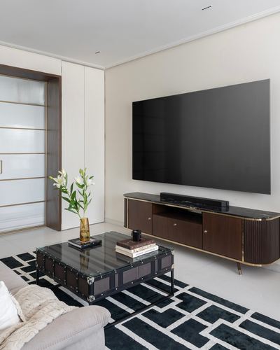 Living room with wall-mounted tv above dark wood console, trunk coffee table on geometric rug