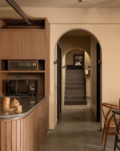 Wooden kitchen counter beside arched doorway leading to a staircase, wishbone chairs at right
