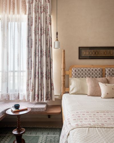 Bedroom with four-poster wooden bed, block-print textiles, pendant light and window seat.