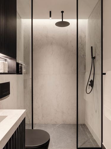Monochrome bathroom with veined stone shower walls, black fixtures, and dark fluted vanity behind glass partition