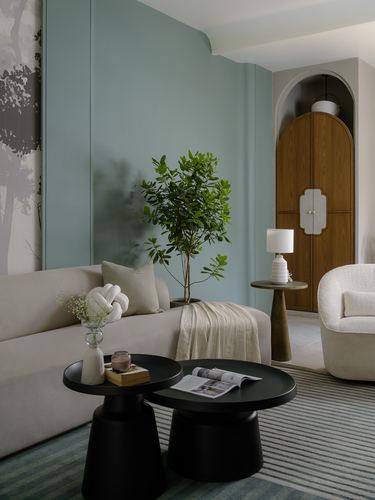 Sage green living room with cream sofa, black nesting tables, and arched wooden cabinet beyond