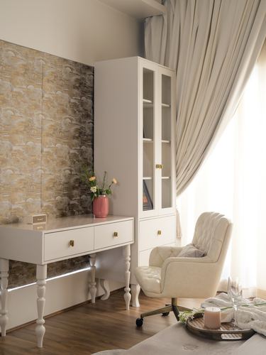 White console and glass cabinet against patterned wall, tufted chair by sheer curtains