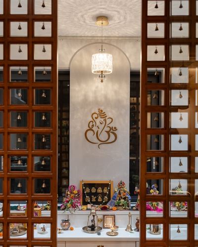 Pooja room framed through carved wooden lattice doors with bells, arched niche and brass idols