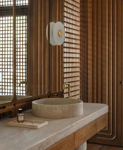Round stone vessel sink on wood-and-stone vanity against a ribbed wood wall with a sculptural sconce