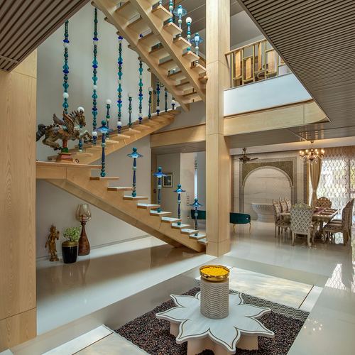Double-height foyer with wooden staircase, beaded railing strings, and flower-shaped stone coffee table