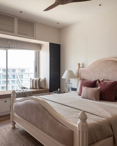 Blush upholstered carved bed facing a window seat in a soft neutral bedroom