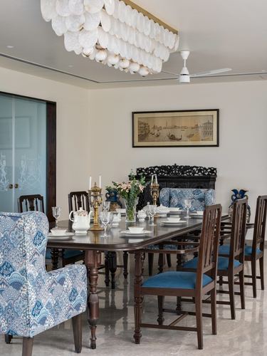 Formal dining room with carved wood panel, blue floral chairs, and a shell chandelier over a long table
