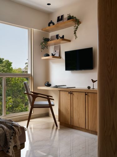 Wood-toned study nook with floating shelves, wall tv, desk, cane chair and marble floor by window