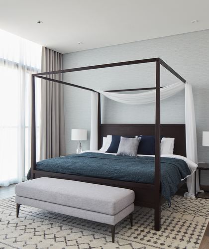 Dark wood four-poster bed with teal bedding and sheer canopy in a neutral, minimalist bedroom