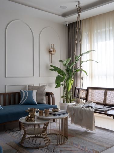 Living room corner with blue daybed, cane hanging swing, arched wall panels and brass tables