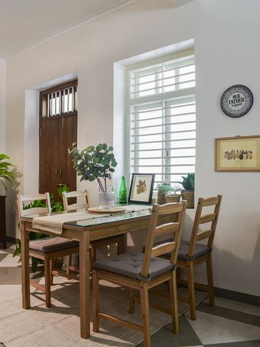 Wooden dining table with four chairs beside a louvered window and framed wall art
