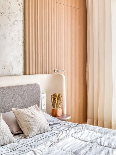 Bedroom corner with fluted wood door, textured plaster wall, and upholstered headboard