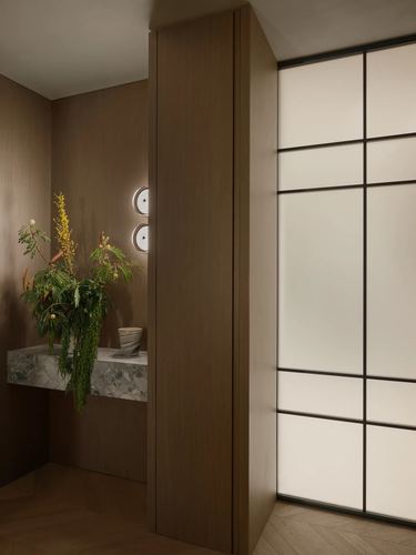 Wood-panelled foyer corner with floating stone console, plant, and backlit glass partition