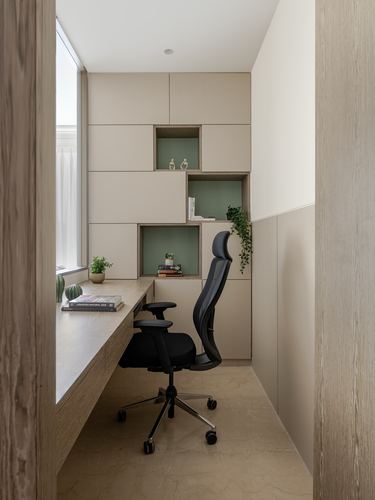 Compact home office nook with beige cabinetry, green fluted niches, and black ergonomic chair at window desk