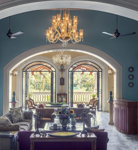 Teal-walled colonial hall with crystal chandelier framed by arched doorway to balcony