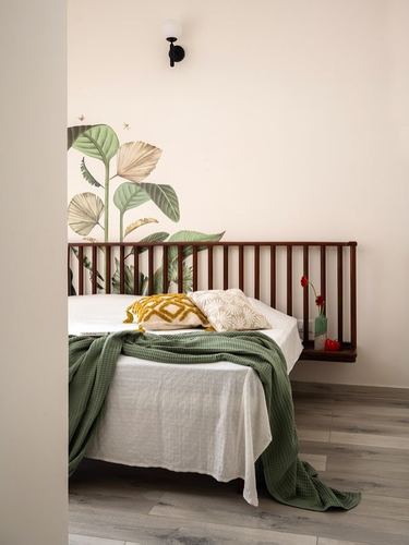 Bed with slatted wood headboard against wall painted with tropical leaf mural, green throw and cushions.