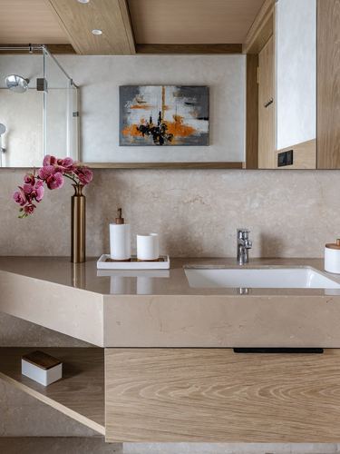 Beige stone vanity counter with sink, brass vase of orchids, and abstract painting above