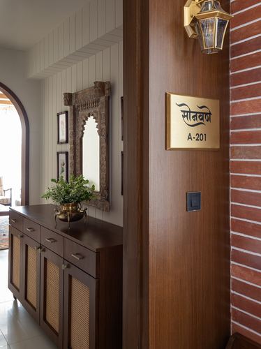 Foyer with carved wooden mirror, cane sideboard, and brass nameplate on wood door beside brick wall
