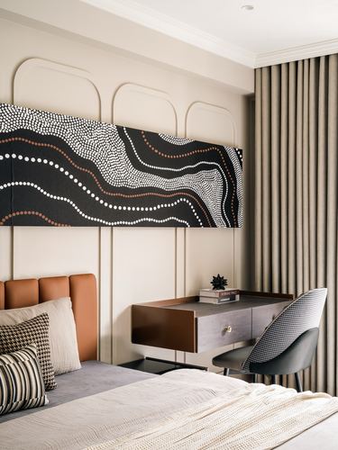 Beige bedroom with tan leather headboard, floating desk, houndstooth chair and dotted black-white artwork