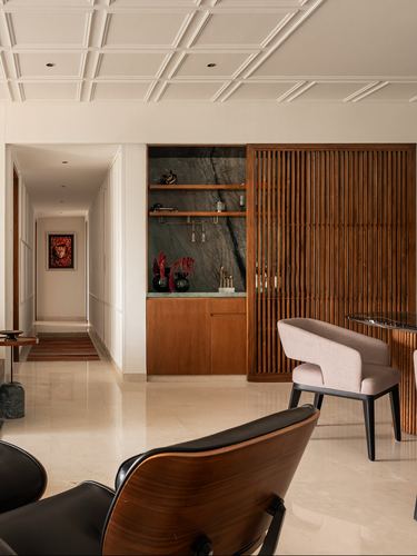 Living room with fluted wood screen, marble display niche, and lounge chairs on stone floor