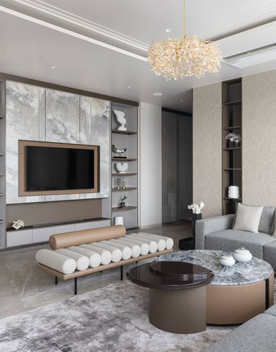 Living room with stone TV wall, cane-style bolster bench, and round marble coffee table under a crystal chandelier