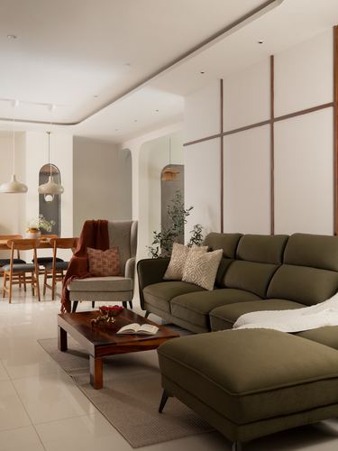 Living room with olive green sectional sofa, wooden coffee table, and paneled accent wall opening to dining area