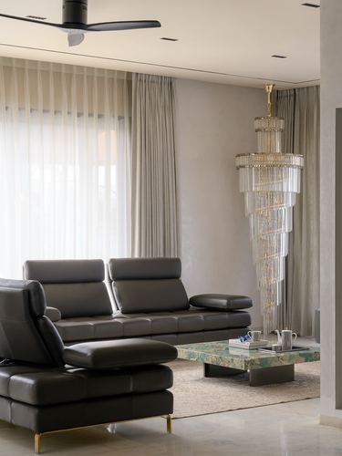 Grey leather sectional sofa facing a tall crystal chandelier beside sheer curtained window