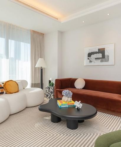 Living room with cream cloud sofa, terracotta velvet couch, and curved black coffee table on striped rug