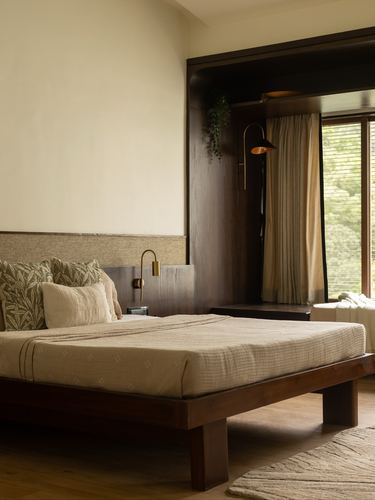 Low wooden platform bed with linen bedding beside a dark wood wardrobe and window with sheer curtains