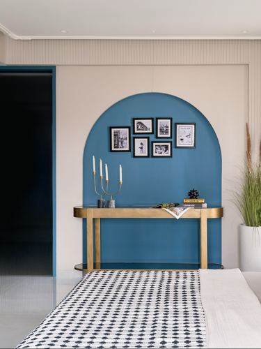 Blue arched niche with brass console and gallery wall behind a patterned bed